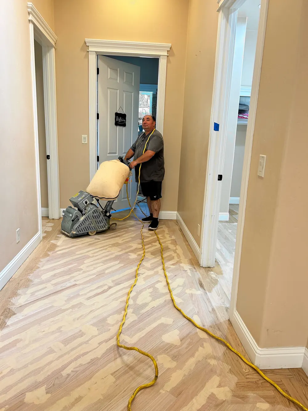 Daniel standing behind a drum sander in a hallway, partway through sanding the floor