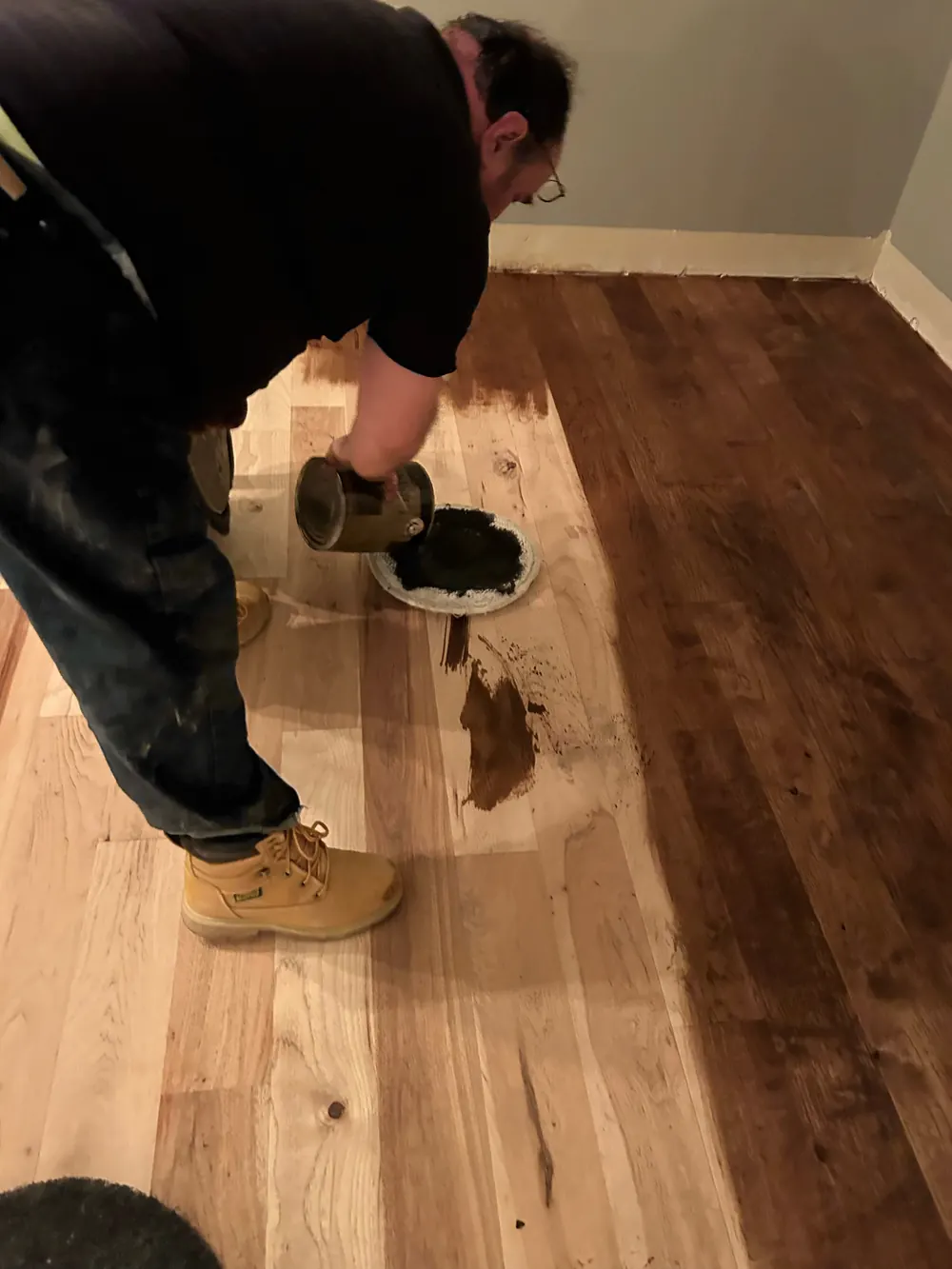 Daniel pouring dark stain from a can onto a freshly sanded hickory floor
