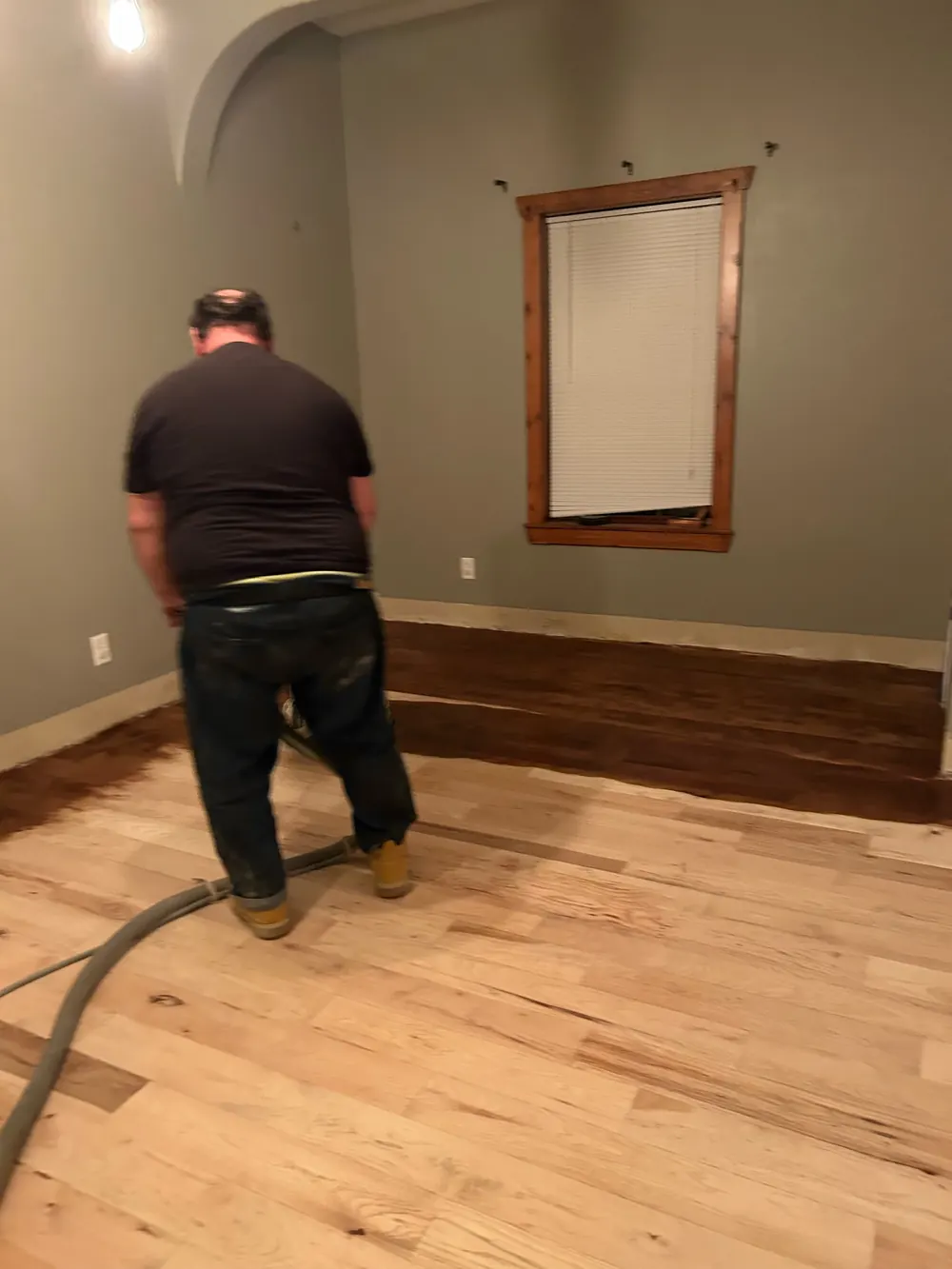 A man standing on a sanded hickory floor, with dark stain started along the far wall