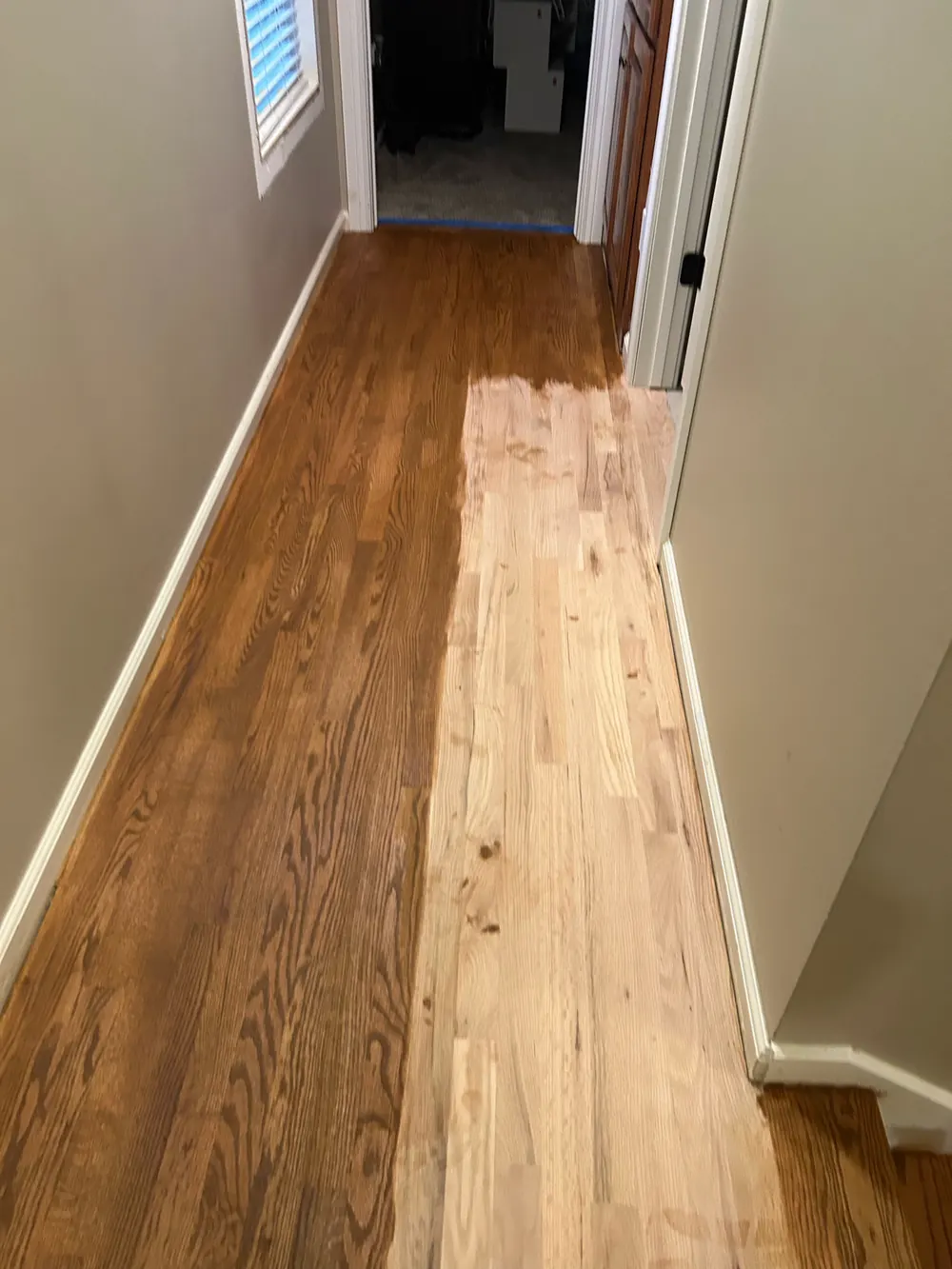 Oak hallway mid-refinish: the left side finished in a warm amber stain, the right side sanded back to bare wood