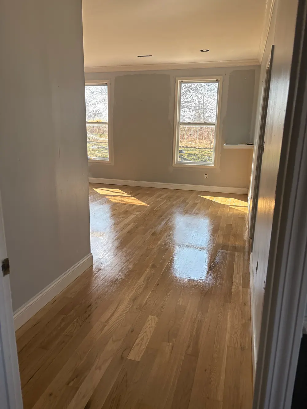 Natural oak strip floor with a glossy finish, light from two windows reflecting across the boards