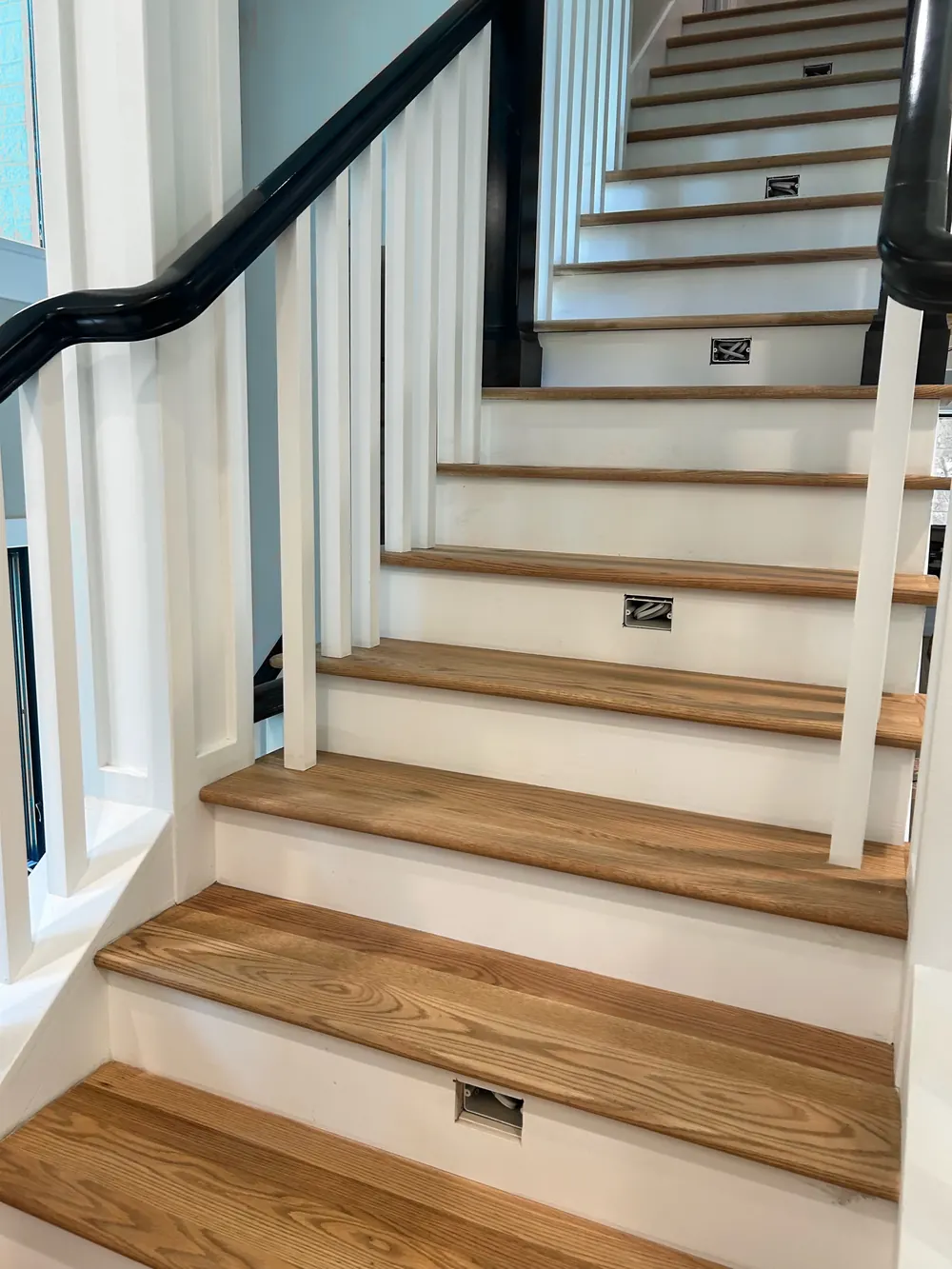 Oak stair treads with white risers, white balusters and a black handrail