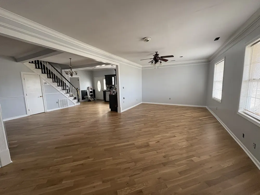 Open great room with a medium-brown hardwood floor and a staircase in the background