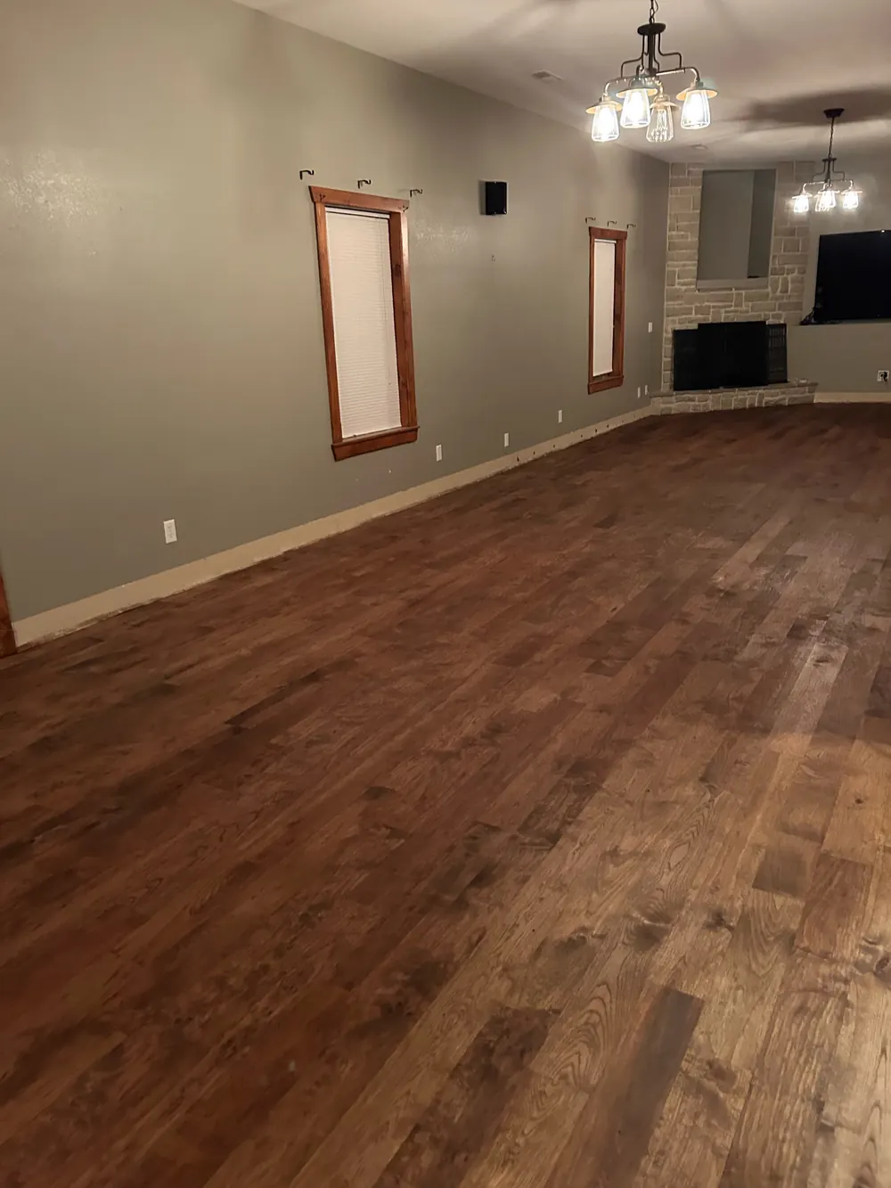 A finished hickory floor in a dark brown stain with the grain still visible, stone fireplace beyond