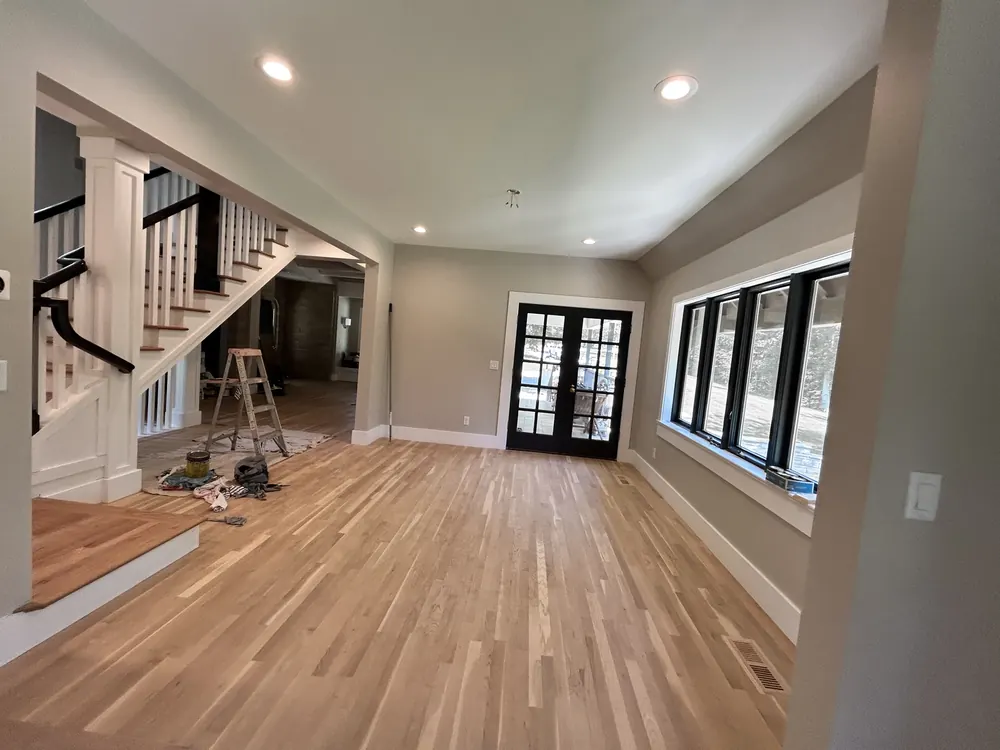 Open entry room with a natural white oak floor, black French doors and a large window wall